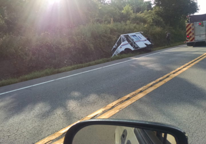 a postal truck lies on its side in a ditch by the side of a road
