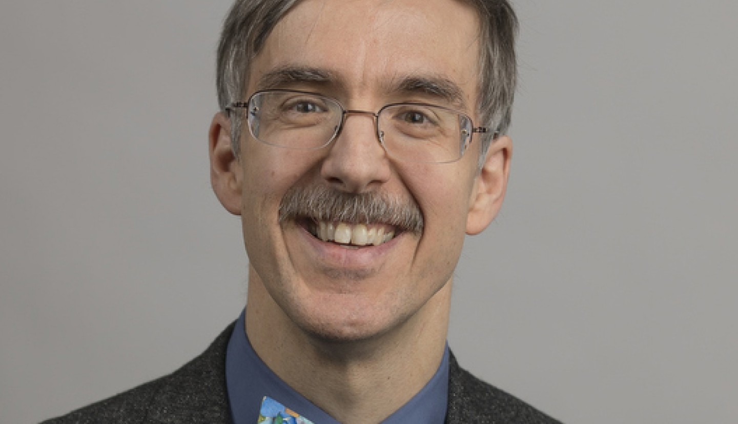 A person with glasses, a blue bow tie and gray suit jacket smiling