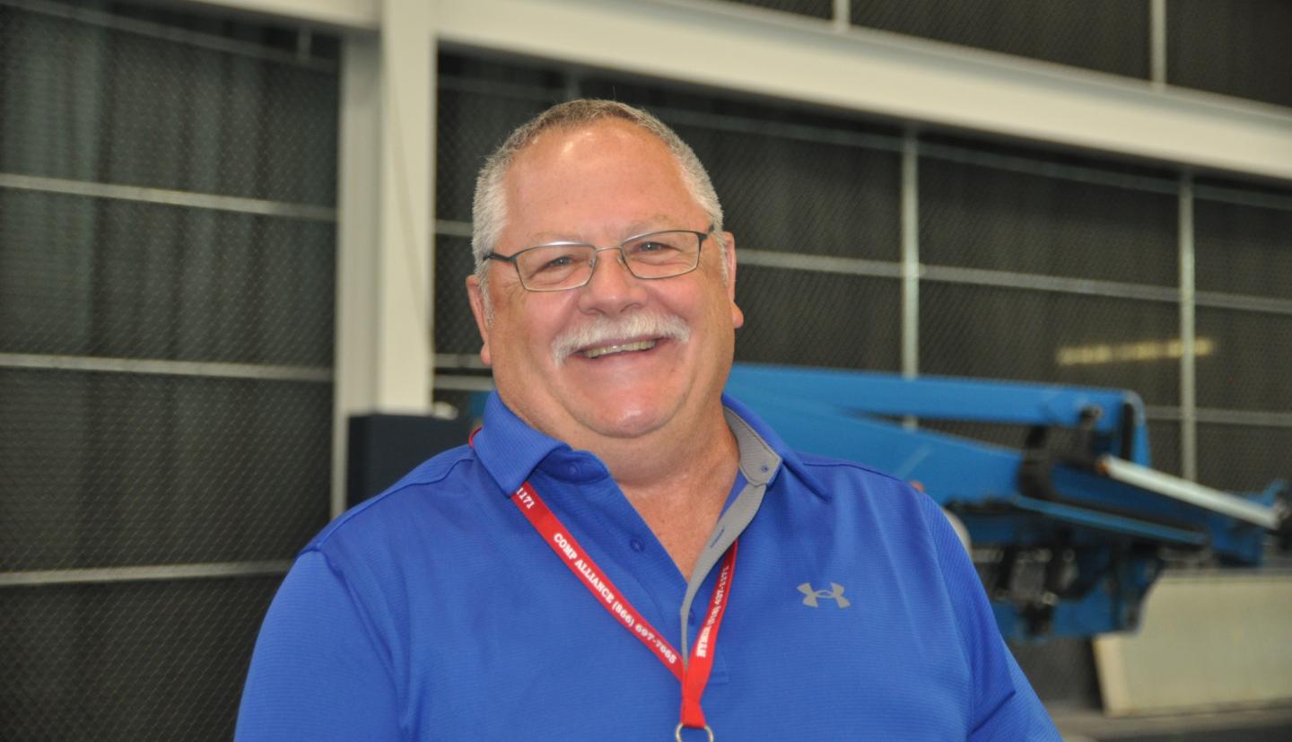 A man wearing a blue shirt and glasses smiling for a photo