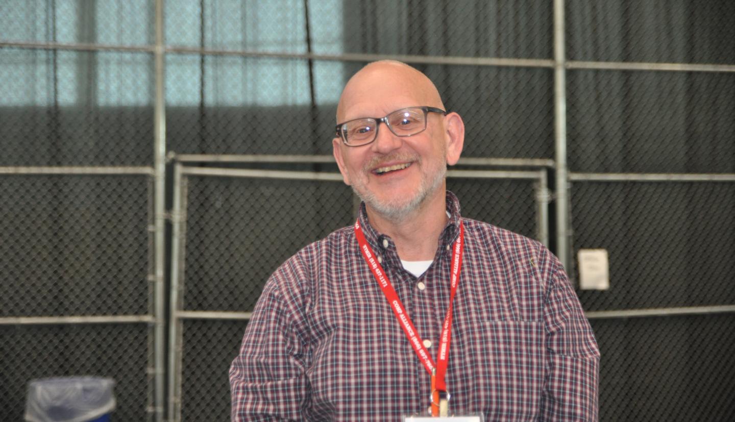 A male in a red and white plaid shirt wearing glasses and smiling at the camera