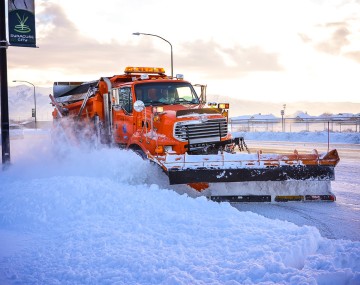 Orange snowplow plowing snow off the road