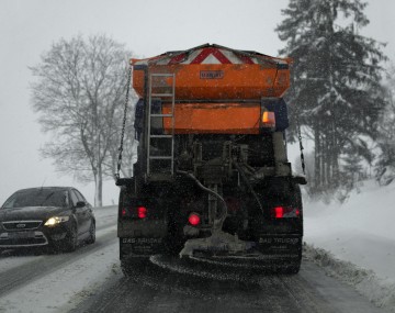Back of an orange snowplow spreading salt on a wintery day 